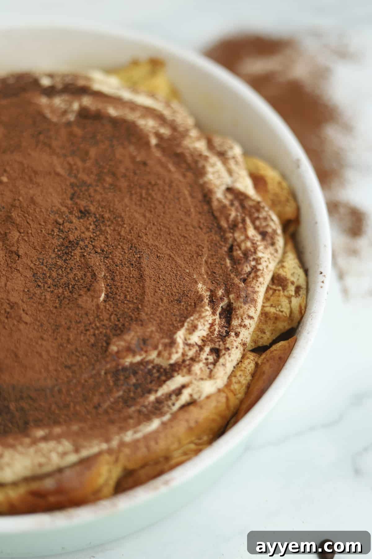 A close-up view of Tiramisu Bread Pudding in a baking dish, showcasing the creamy mascarpone topping and dusted cocoa.