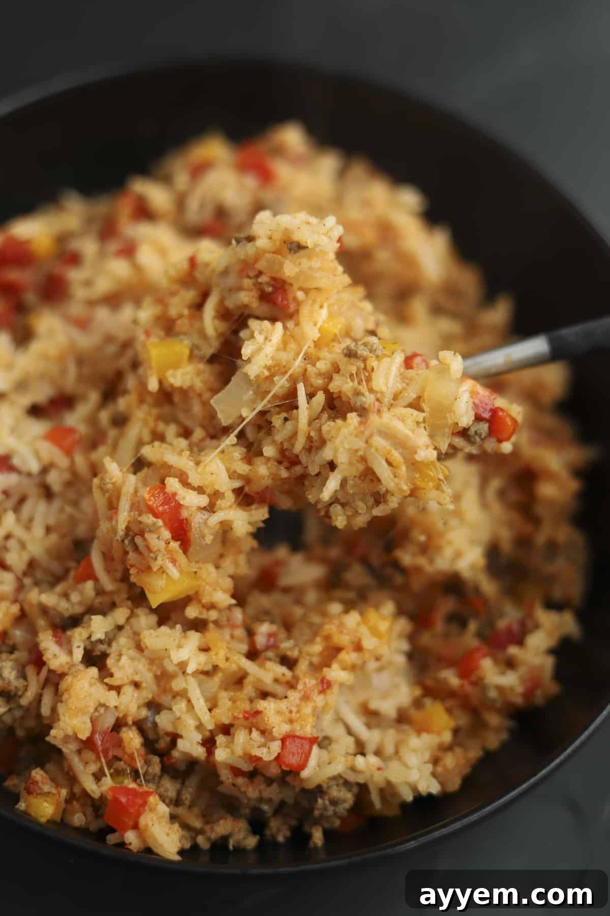 A spoonful of delicious Stuffed Pepper Rice Bake being lifted from a baking dish, showcasing its rich textures.