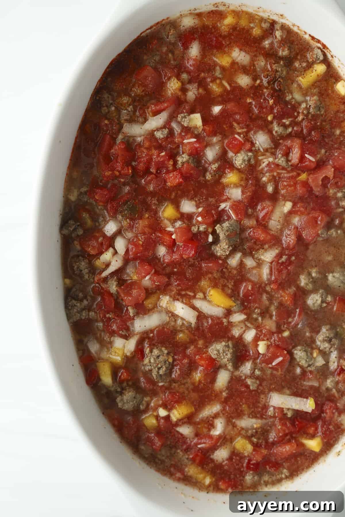 A baking dish filled with colorful ingredients including diced tomatoes, vibrant bell peppers, and browned ground beef, ready for baking.