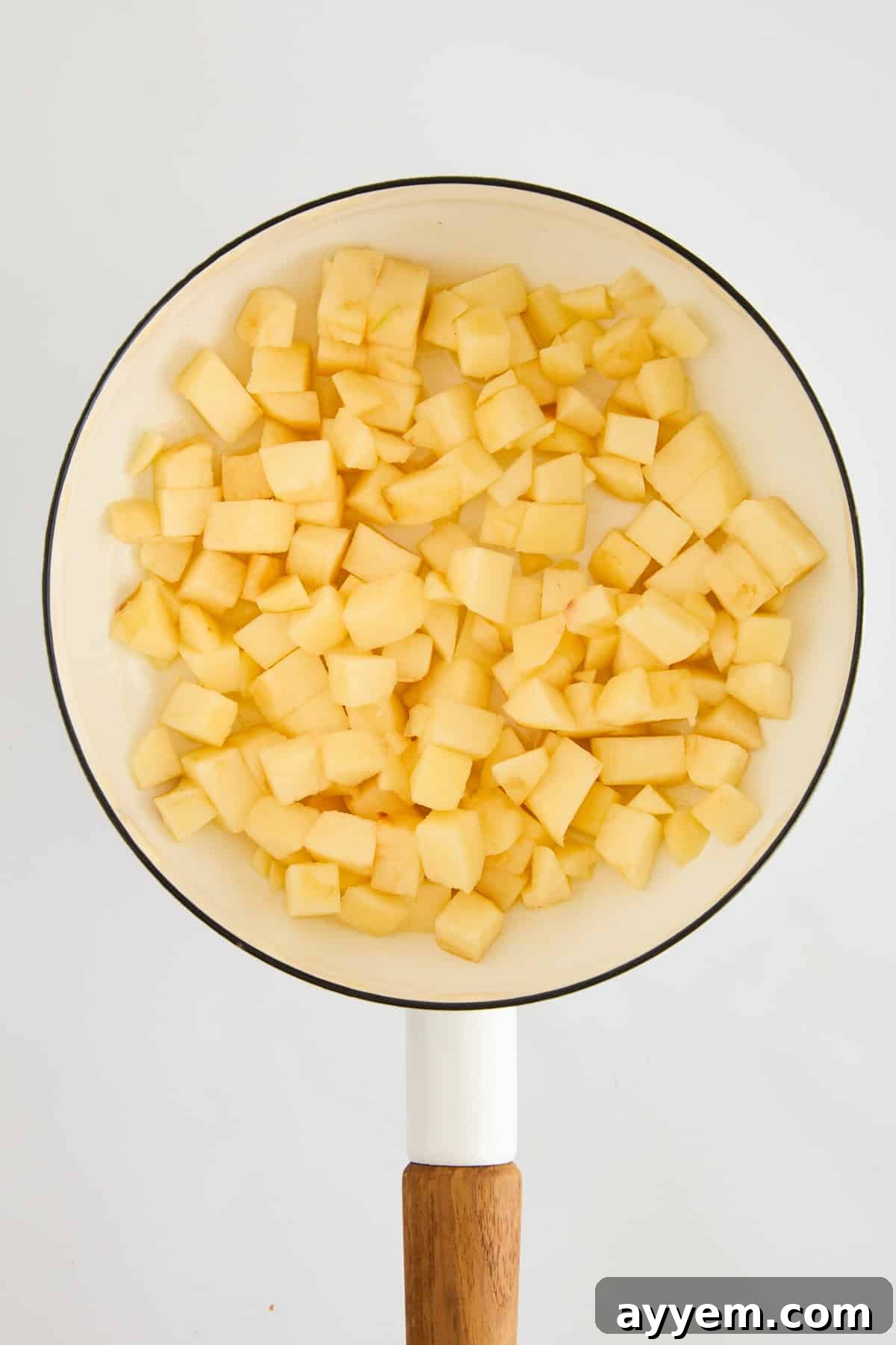 A close-up of diced apples cooking in a pot with butter, brown sugar, cinnamon, and nutmeg.