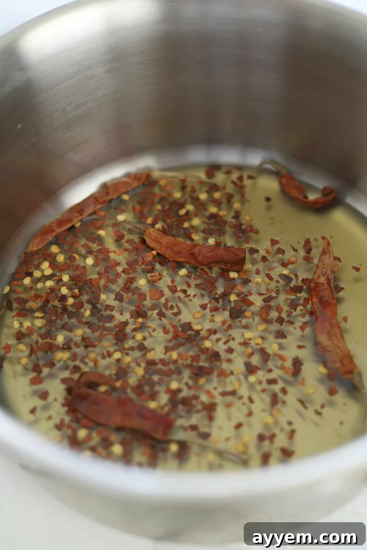 A small pot containing golden honey infused with vibrant red pepper flakes and dried chili peppers, simmering gently on a stovetop, capturing the essence of homemade hot honey preparation.