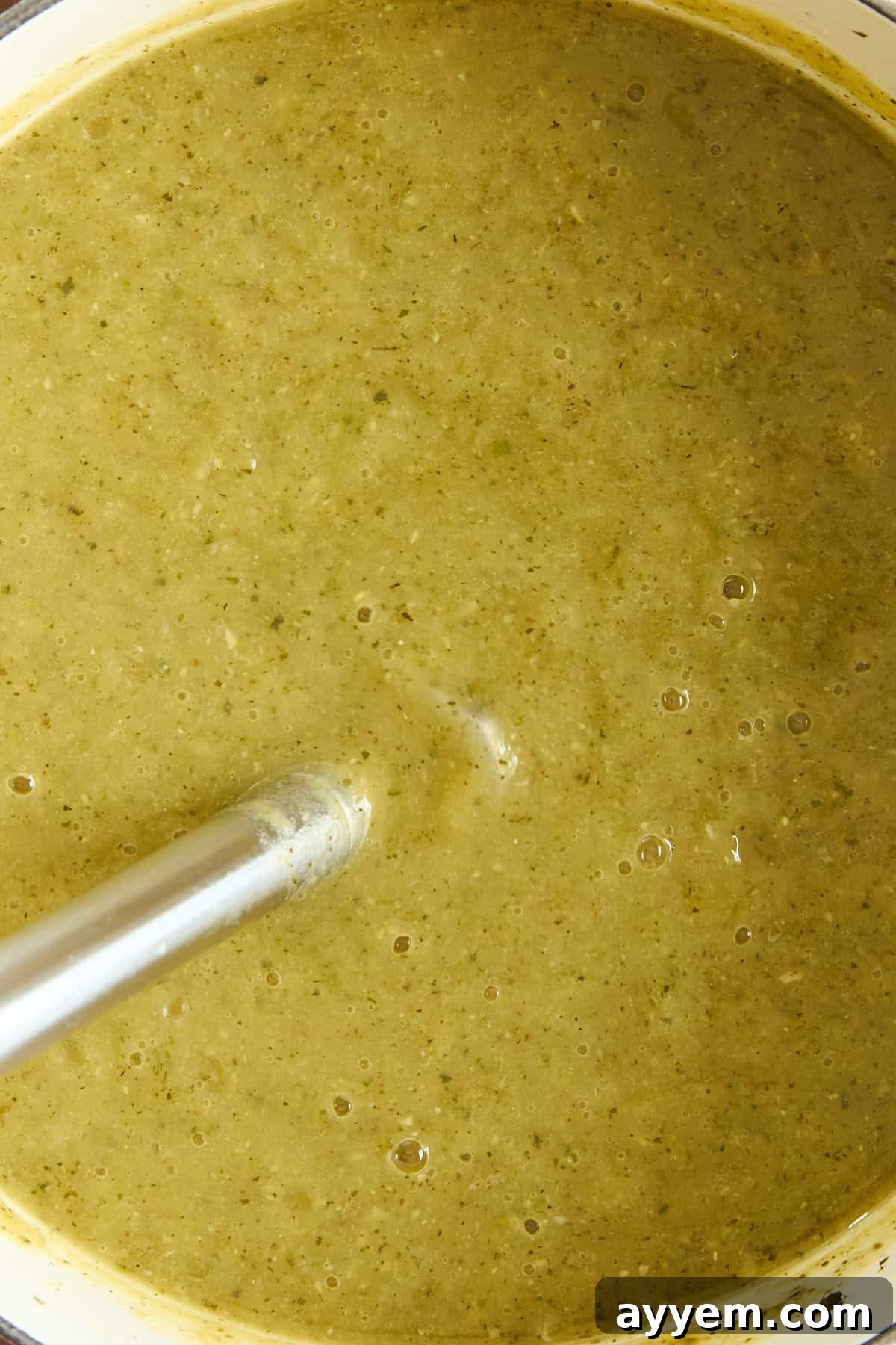 An immersion blender skillfully puréeing a pot of vibrant green vegetable soup, effortlessly creating a smooth, luxurious, and creamy texture that is irresistible.
