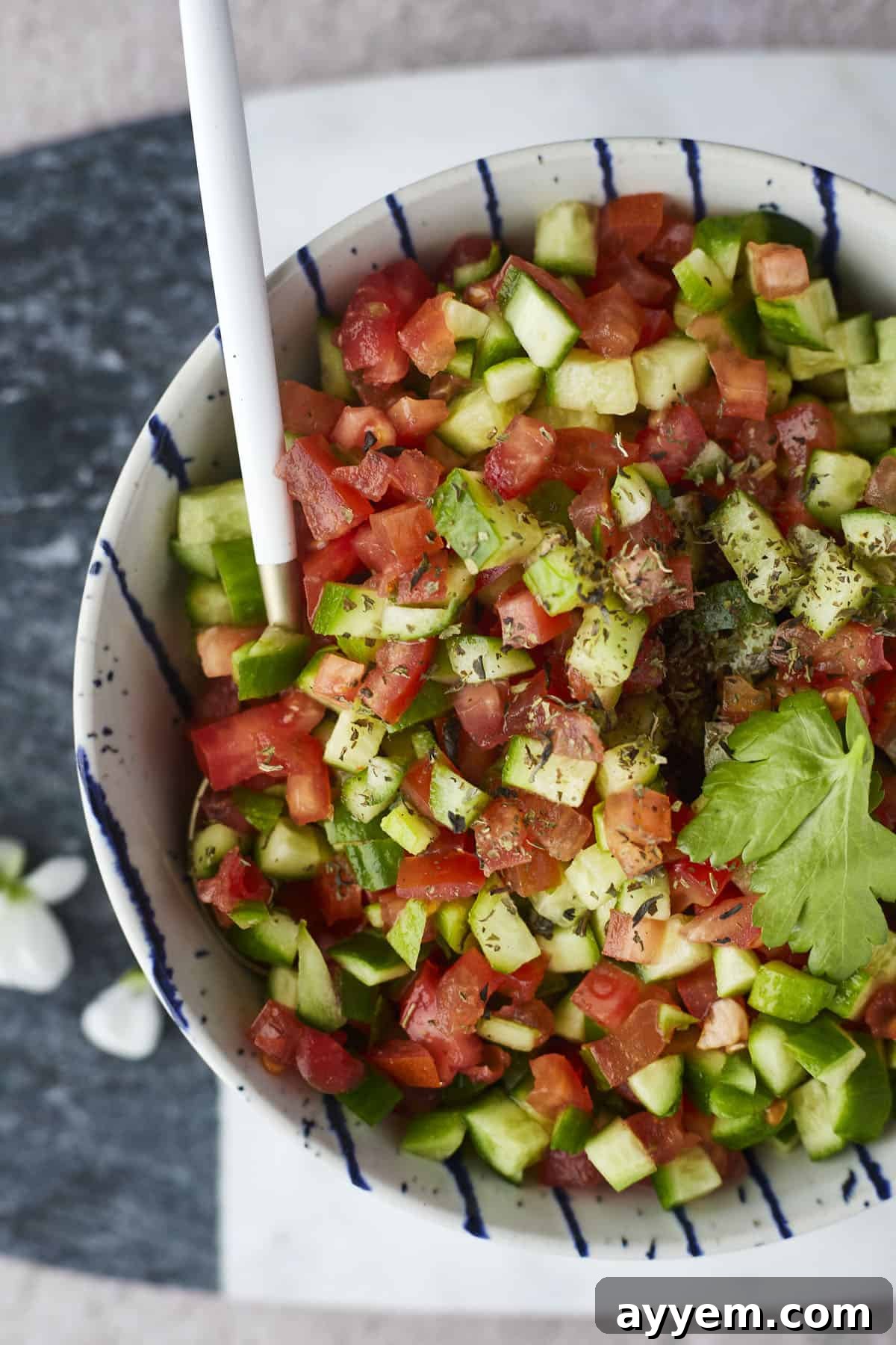 A close-up shot of Egyptian Tomato & Cucumber Salad being gently tossed with a spoon in a clear glass bowl, highlighting the fresh, vibrant ingredients.