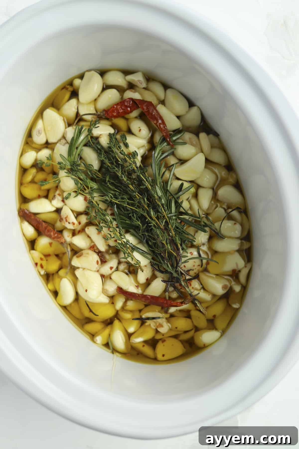 Overhead view of slow cooker spicy honey garlic confit with fresh herbs, ready to be cooked.