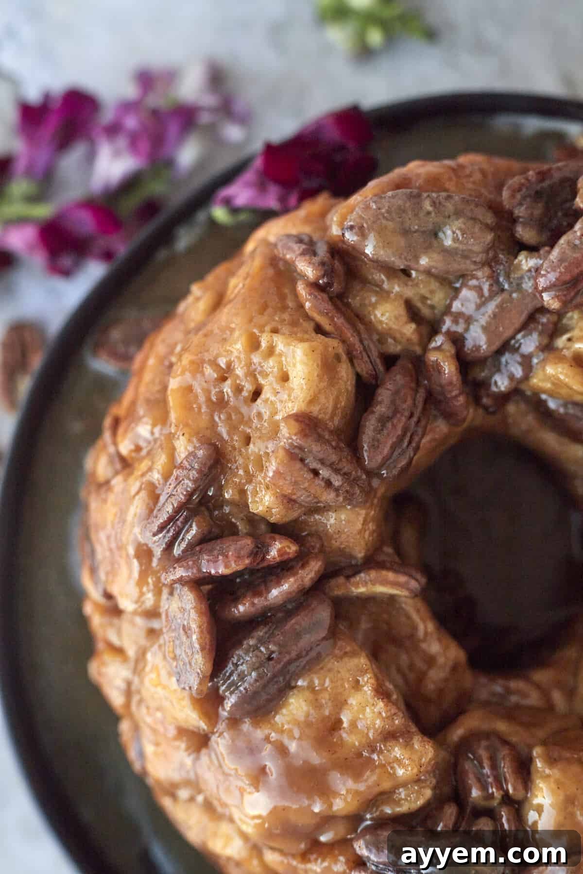 A beautifully baked ring of pecan caramel homemade monkey bread, glistening with caramel, served on a white plate, ready to be pulled apart and enjoyed.
