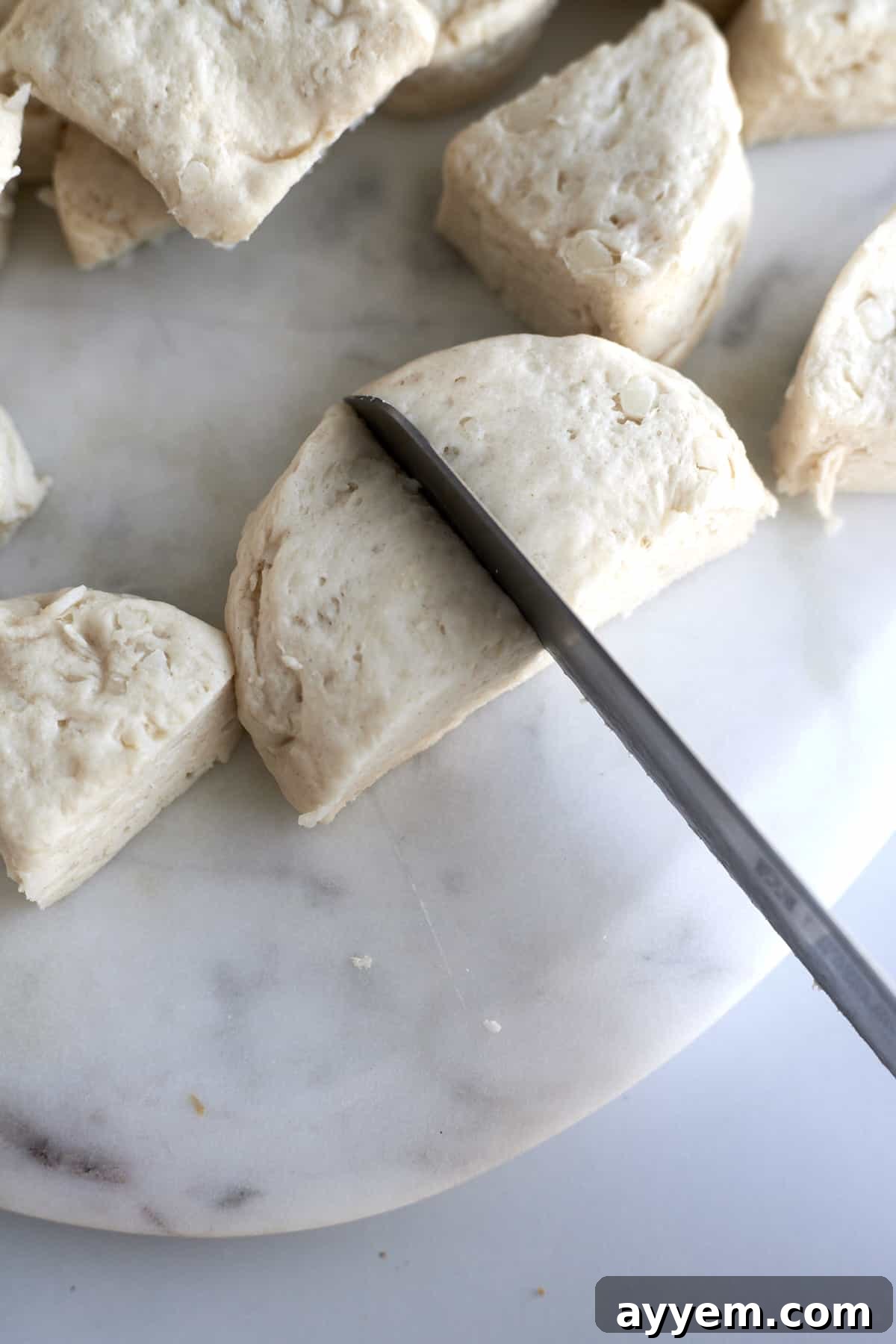 Raw biscuit dough being quartered on a cutting board, preparing for the monkey bread assembly. Each piece is destined to be coated in caramel and pecans.