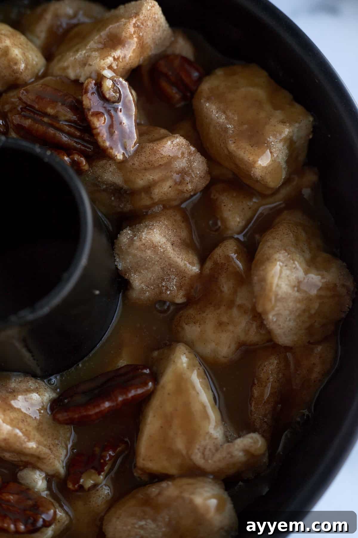 Pecan caramel monkey bread baking in a bundt pan, showing a golden top and bubbling caramel sauce.