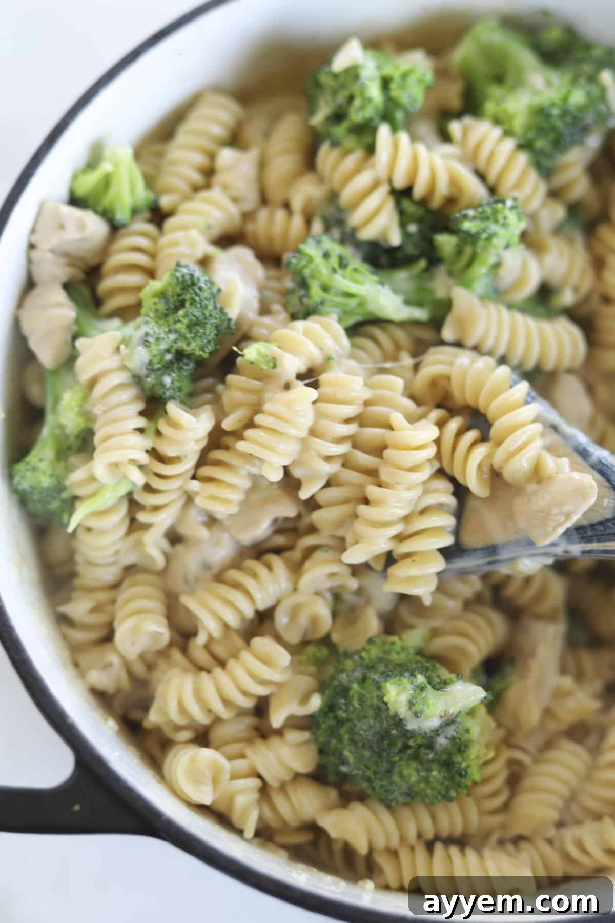 A large pot filled with creamy chicken, broccoli, and rotini pasta, garnished with fresh herbs and Parmesan cheese.