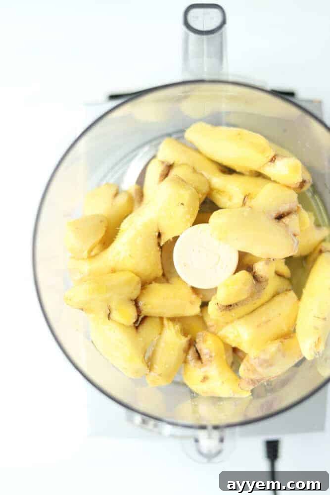 Close-up overhead view of fresh ginger being peeled and prepared in a food processor, ready for use or storage.