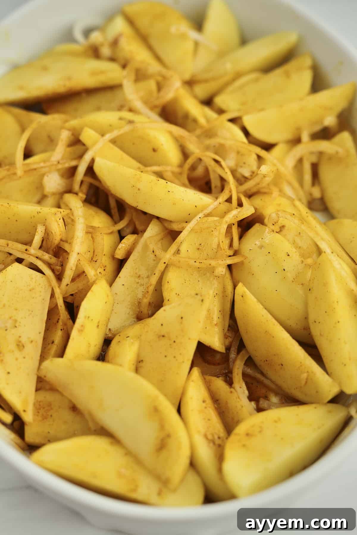 Raw potato wedges and thinly sliced onions arranged in a baking dish, ready for seasoning.