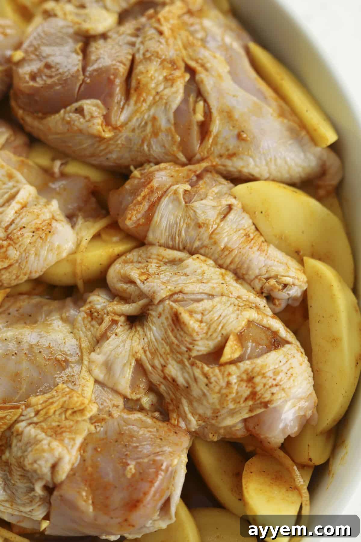 Raw chicken pieces, seasoned potatoes, and onions mixed with the vibrant Middle Eastern marinade in a baking dish.