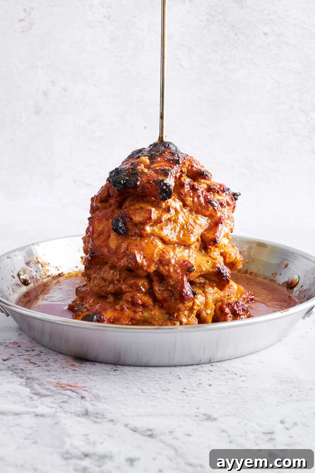 Beautifully baked chicken shawarma on a vertical spit, golden brown and perfectly cooked, with thin slices already carved from the savory meat.