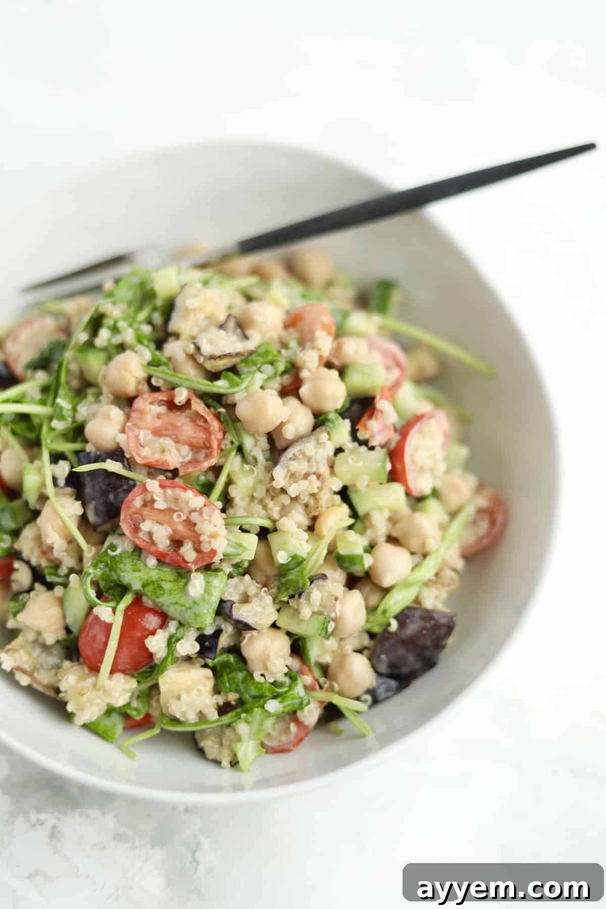 Vegan roasted eggplant salad in a white bowl with tahini dressing, quinoa, and a chopstick