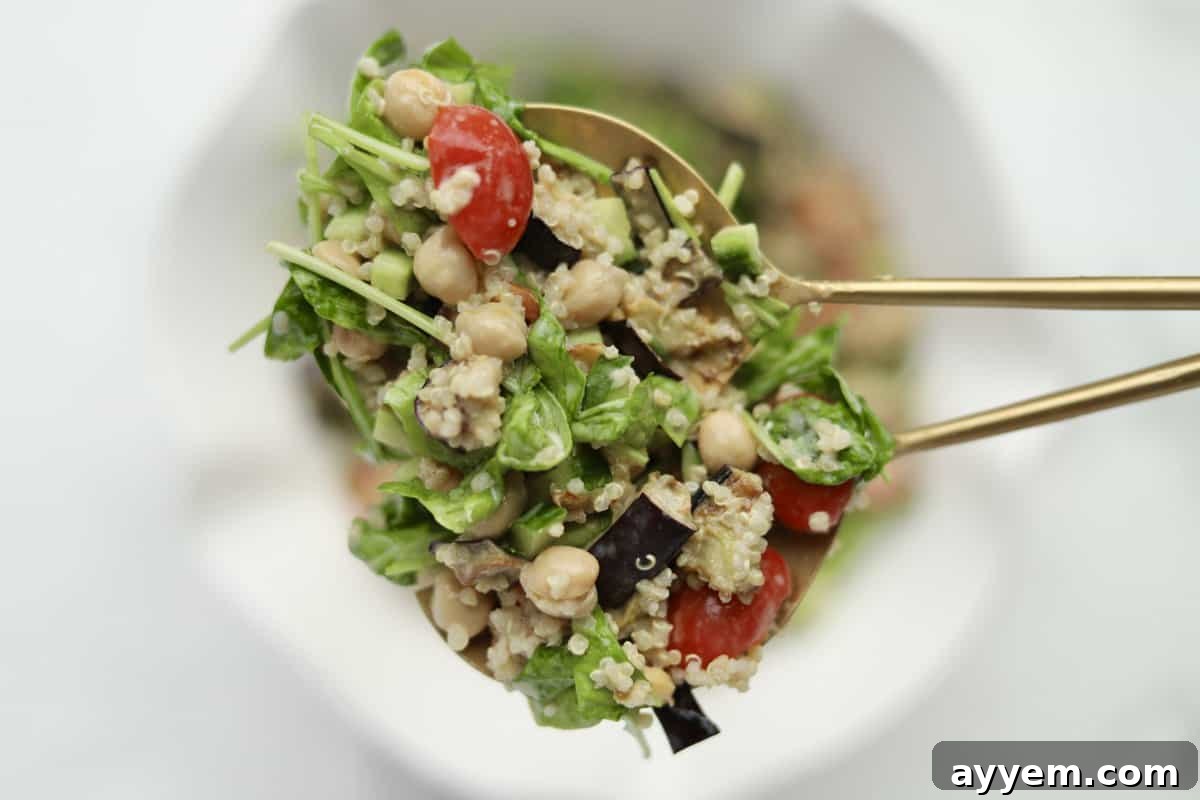 Two gold chopsticks holding a bite of vegan roasted eggplant salad coated with tahini dressing