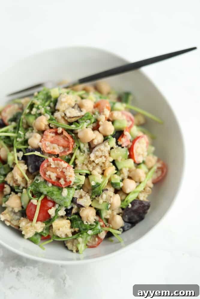Vegan roasted eggplant salad in a white bowl with tahini dressing and quinoa and a chopstick sticking out