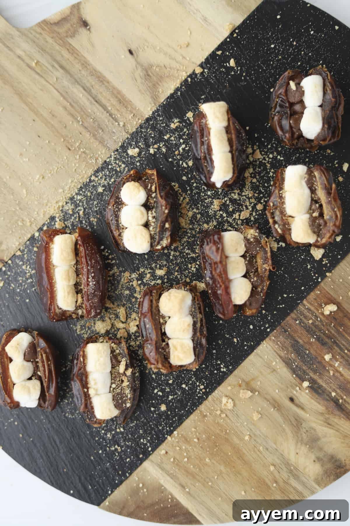 a board full of s'mores stuffed dates, golden brown and garnished with graham cracker crumbs