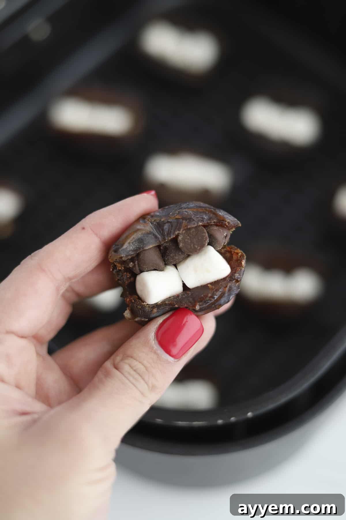 a hand holding two s'mores stuffed dates, showing the gooey filling