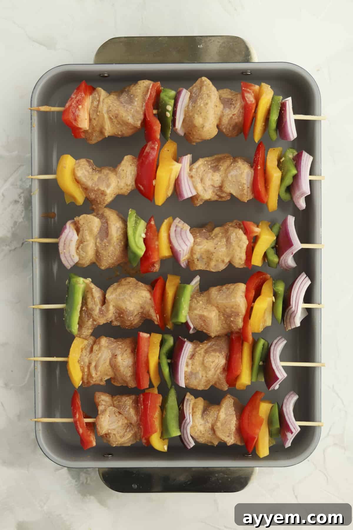 baking dish of raw chicken skewers with veggies