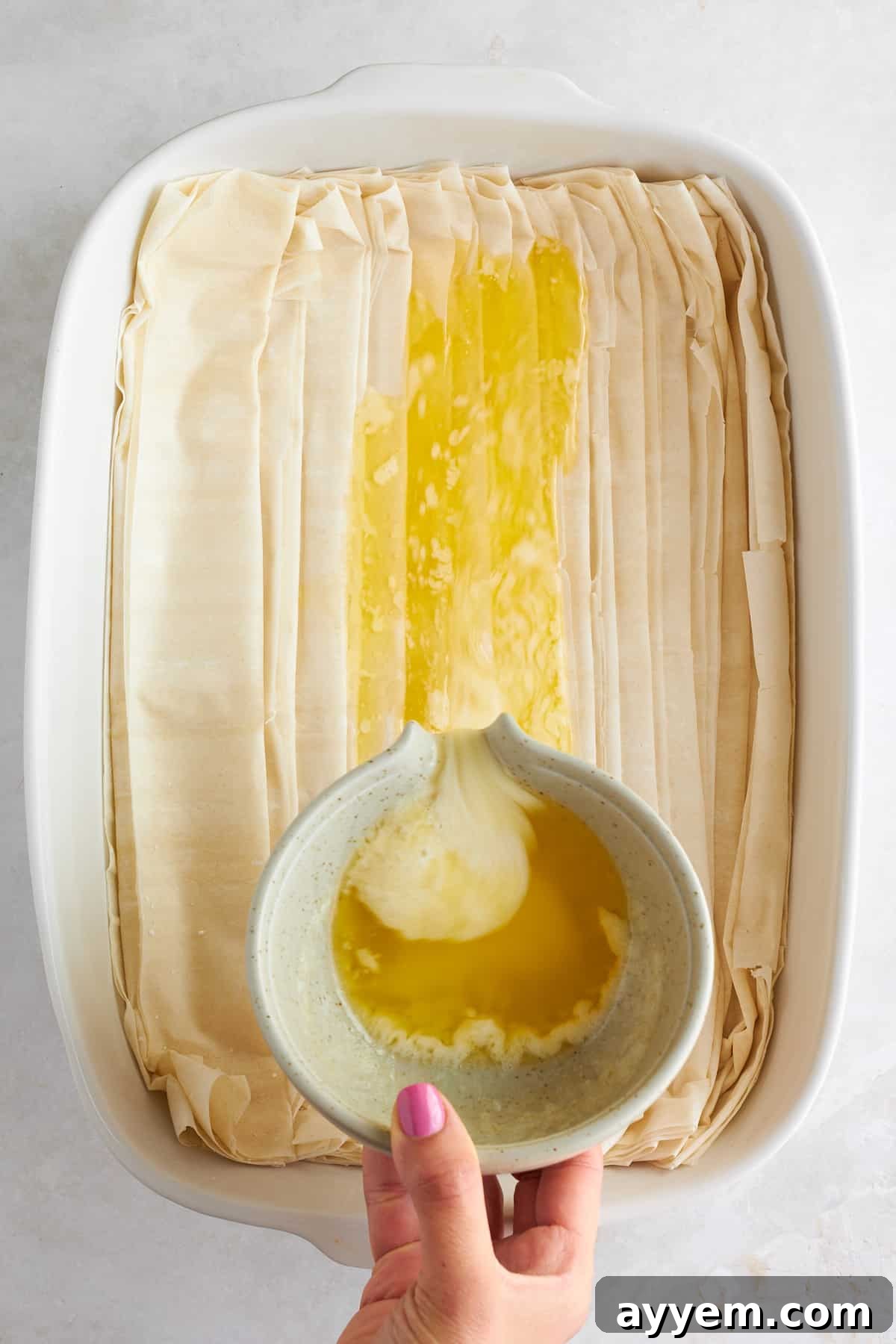Melted butter being poured over crinkled phyllo dough in a baking dish.