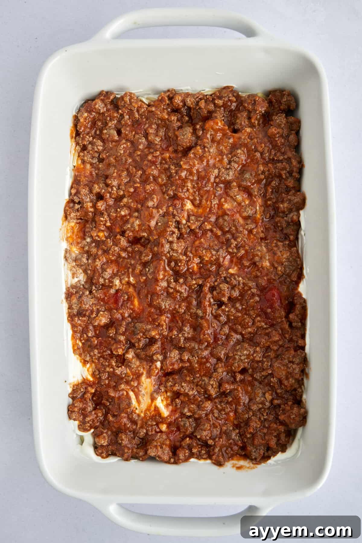 Layers of spaghetti, creamy sauce, and rich marinara meat sauce beginning to take shape in the baking dish.