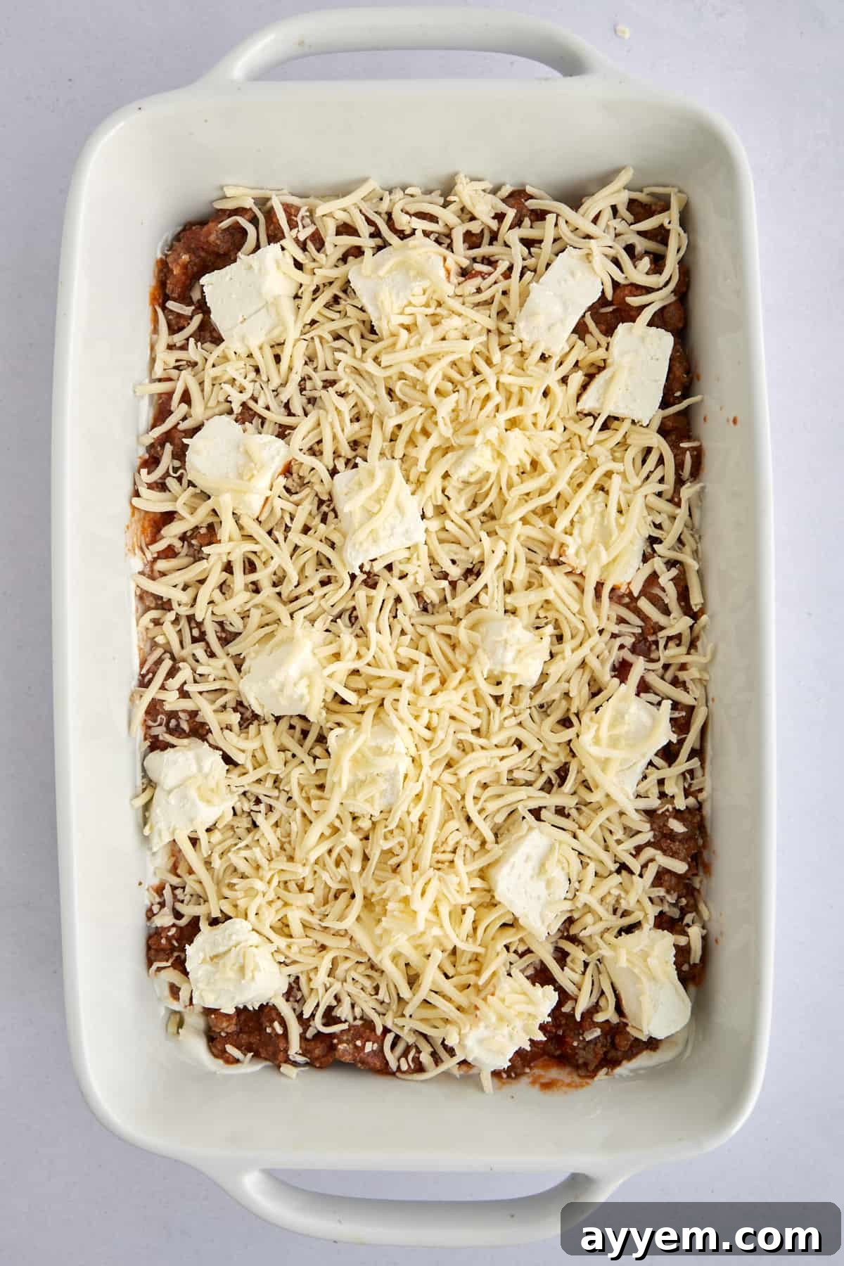 The delicious layers of unbaked Million Dollar Spaghetti, topped with an enticing blend of cheese chunks and shredded mozzarella, promising a golden, bubbly finish.