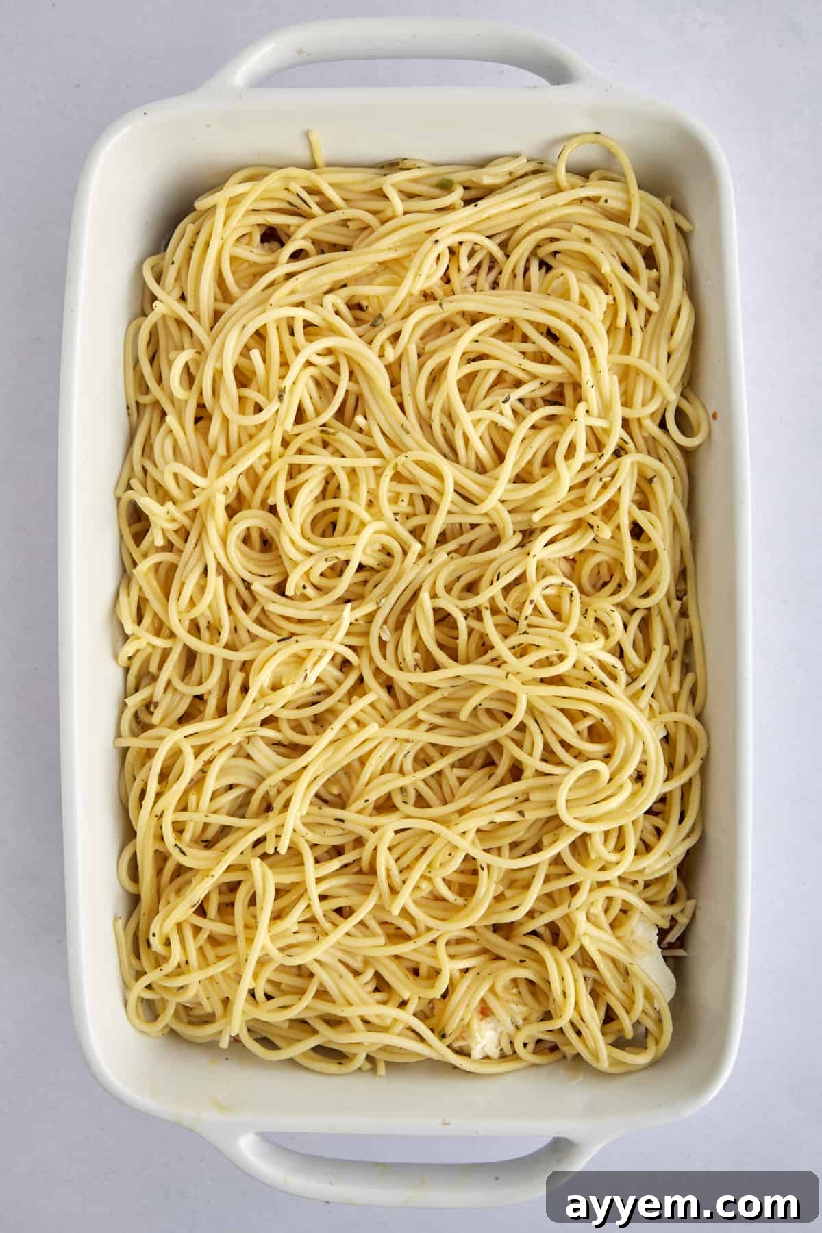 A close-up view of cooked spaghetti noodles forming the base layer in a casserole dish, ready for more savory additions.