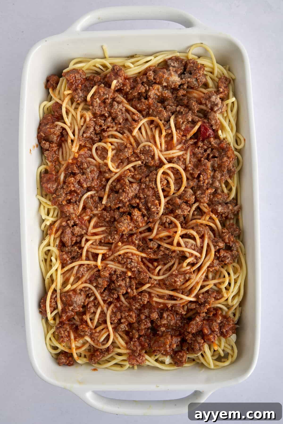 A vibrant layer of marinara meat sauce generously spread over the creamy spaghetti base in the baking dish.