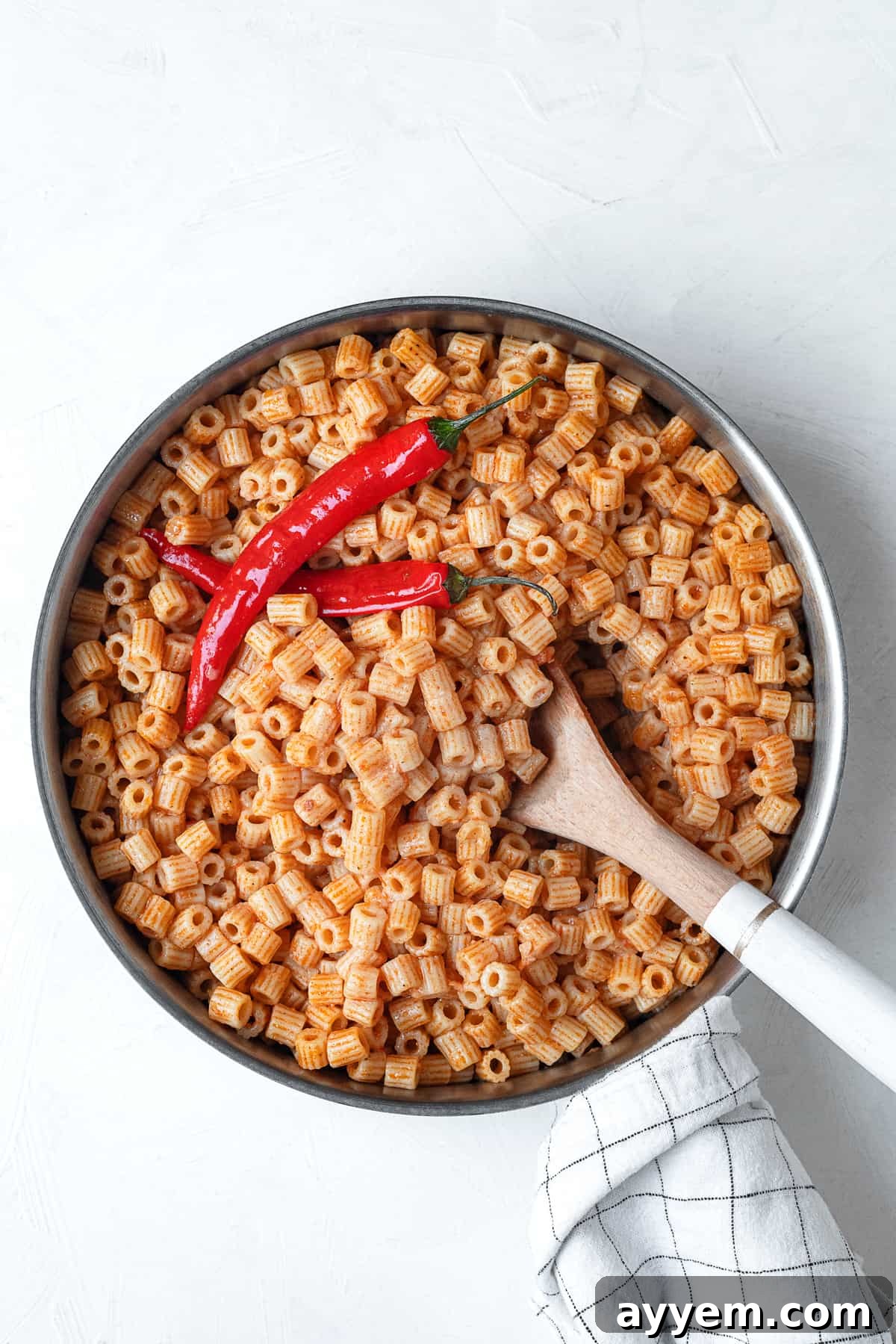 overhead image of one pot mbakbaka topped with peppers being stirred with a spoon