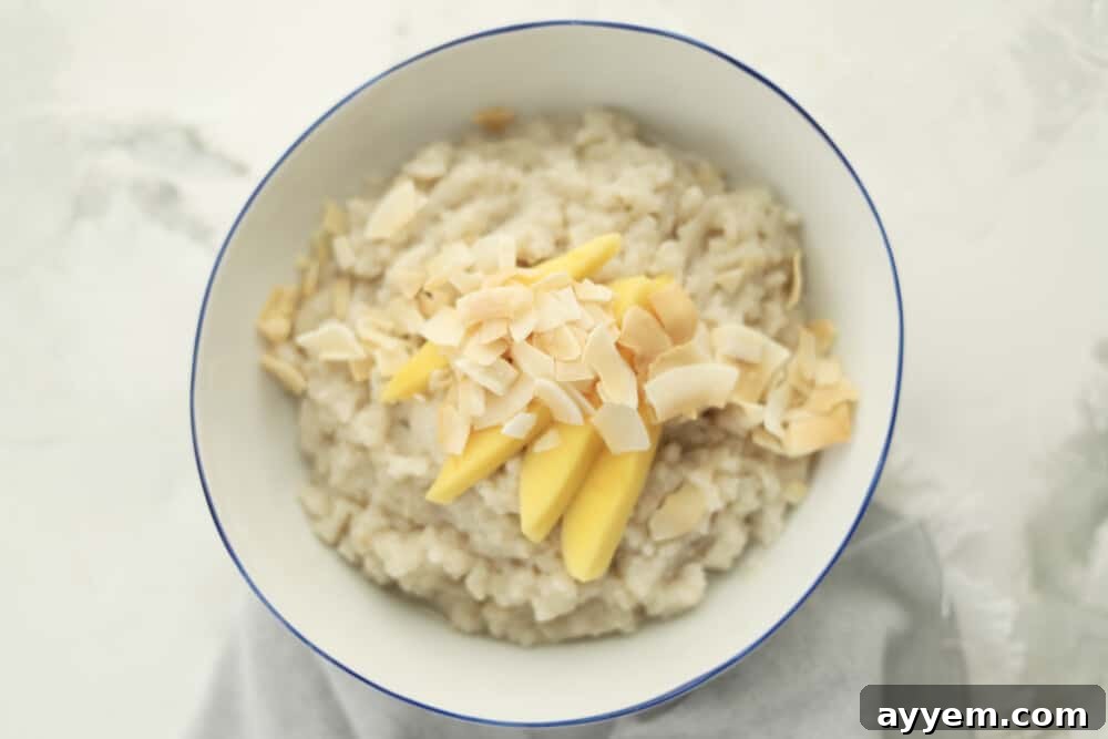 a bowl of slow cooker coconut sticky rice topped with sliced mangoes and coconut flakes