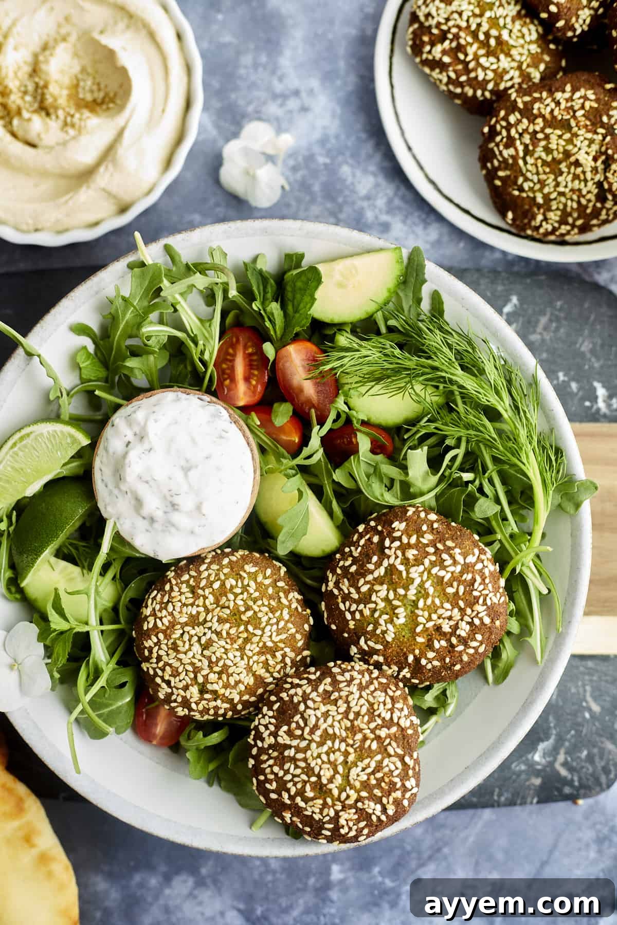 three pieces of falafel over a salad with a small bowl of tzatziki