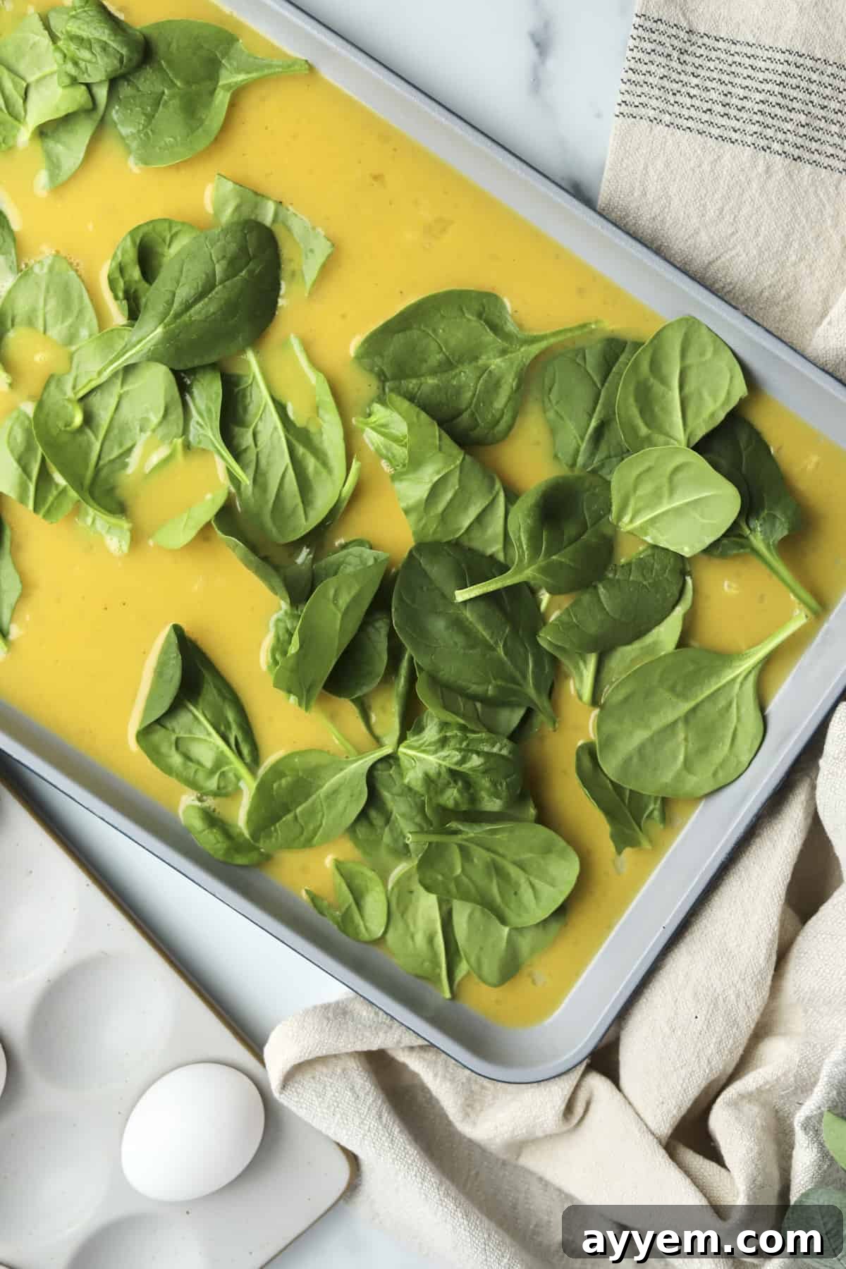 Raw eggs topped with fresh, vibrant spinach in a baking pan, perfectly arranged and ready to be baked into delicious, protein-rich patties.