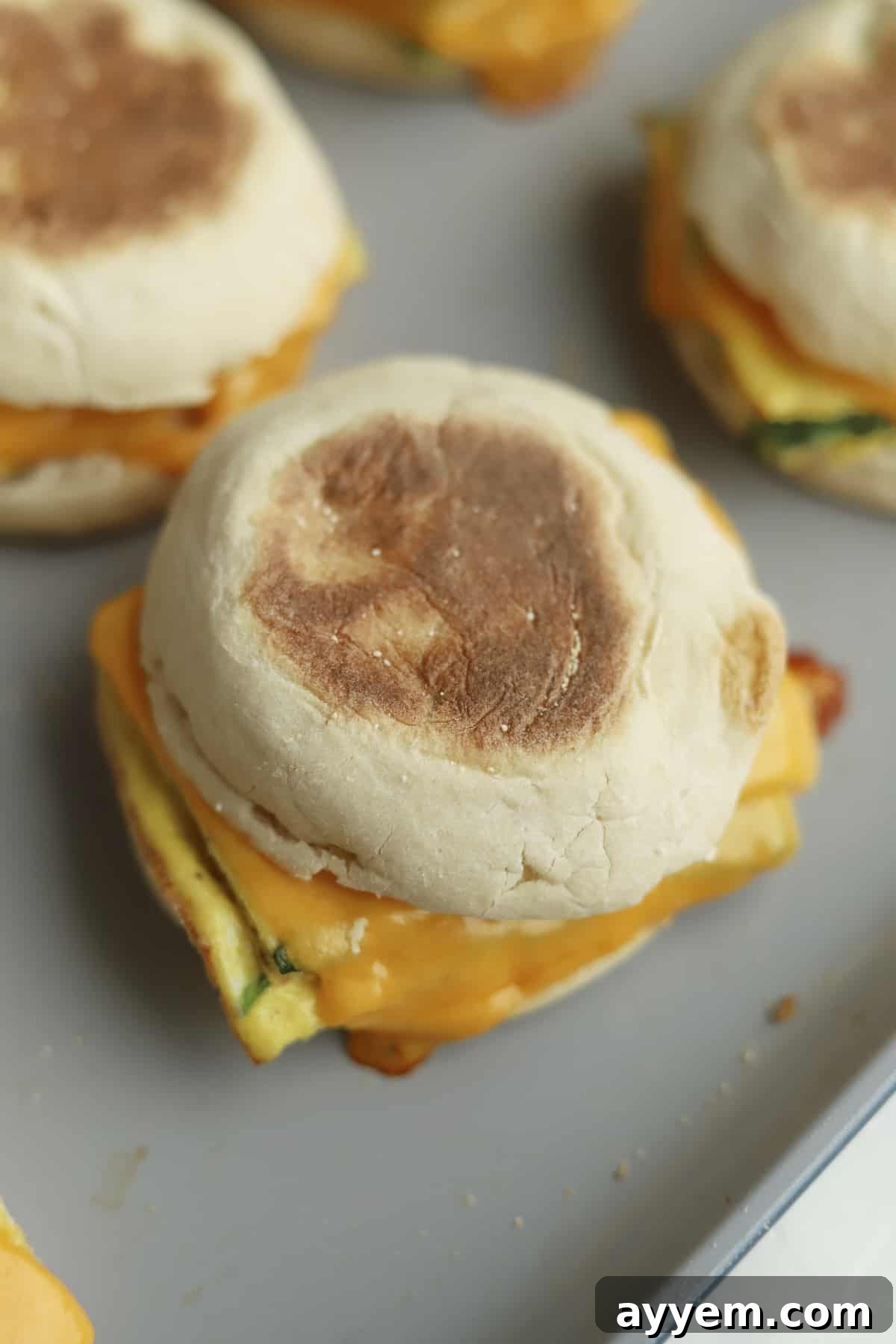 A delectable close-up view of protein-packed egg muffin sandwiches on a baking dish, showcasing the beautifully melted cheese oozing over the fluffy egg patties.