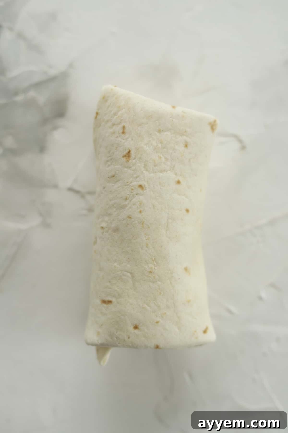 An uncooked strawberry cheesecake chimichanga, perfectly rolled and ready for air frying, showcasing its neat and compact form.