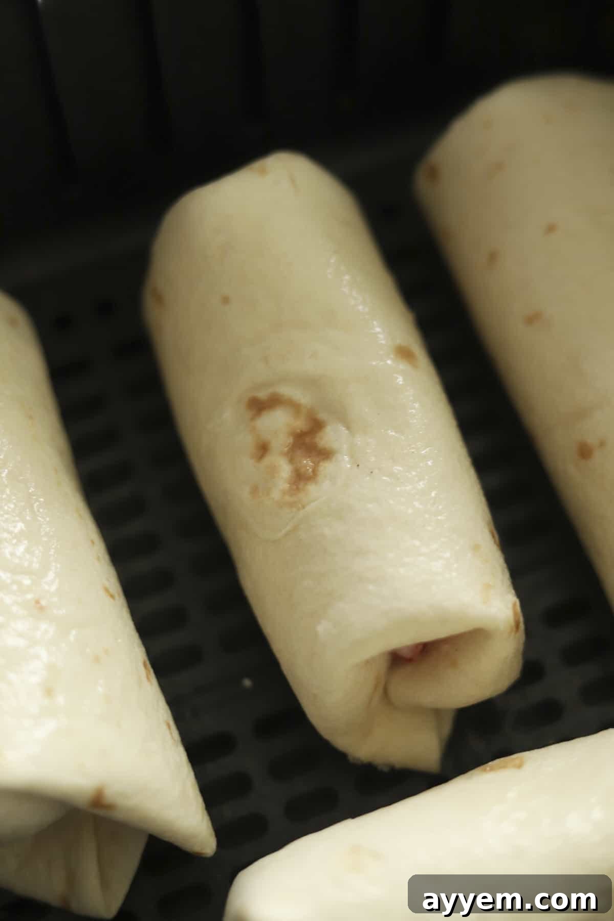 Several strawberry cheesecake chimichangas neatly arranged in an air fryer basket, cooking to a golden crisp.