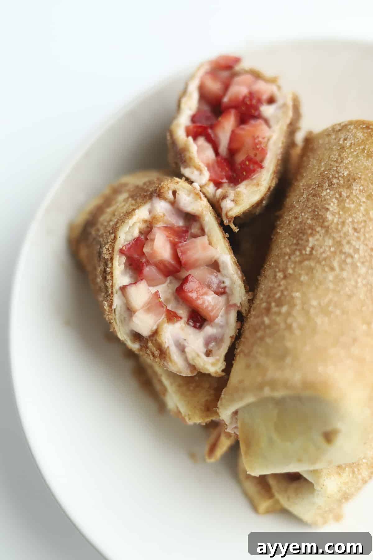 A cross-section of a freshly air-fried strawberry cheesecake chimichanga, showcasing its warm, gooey strawberry cream cheese filling and crispy cinnamon-sugar dusted tortilla. Fresh strawberries are scattered around for garnish.