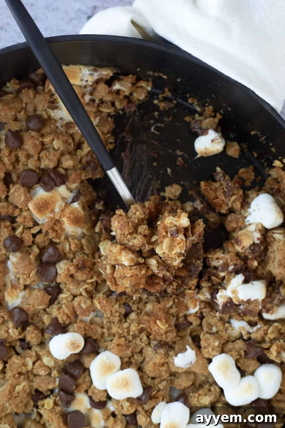 A spoon holding a bit of a S'mores cookie skillet.