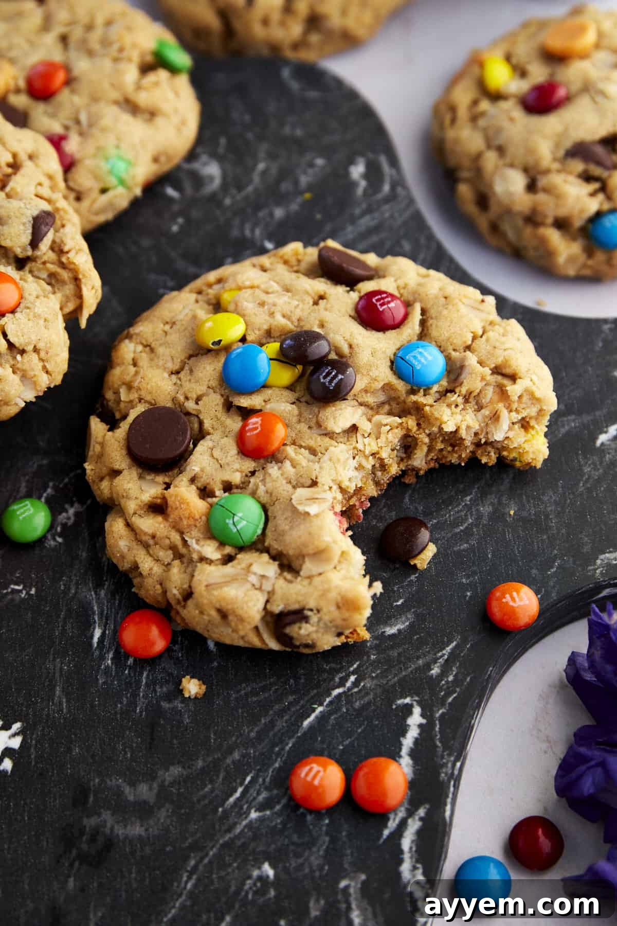 Fully Loaded Monster Cookies 5 A delectable Monster Cookie with a bite taken out, revealing its soft, chewy interior filled with oats, chocolate, and M&M's.