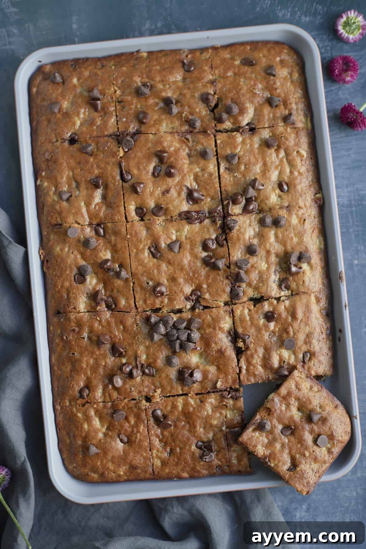 overhead of a banana bread cut into squares on a sheet pan with one off of the pan.