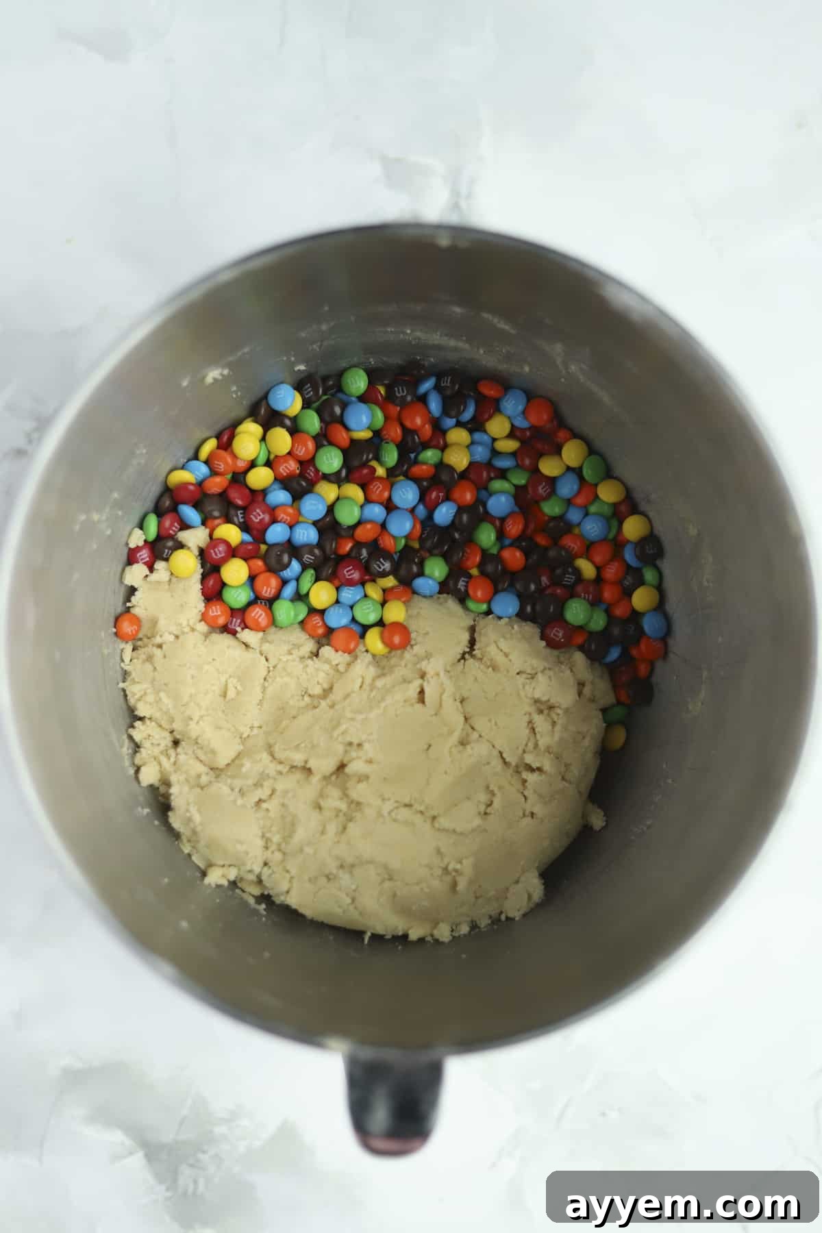 Bowl of a stand mixer with cookie dough and M&Ms, illustrating the mixing process for soft-baked M&M cookies.