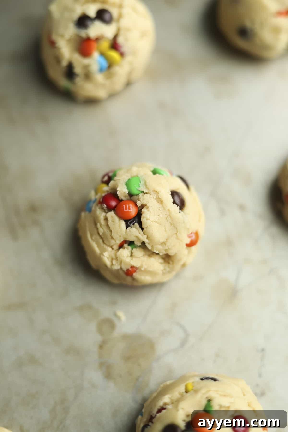 One perfectly portioned cookie dough ball on a baking sheet, ready for the oven to become a soft-baked M&M cookie.