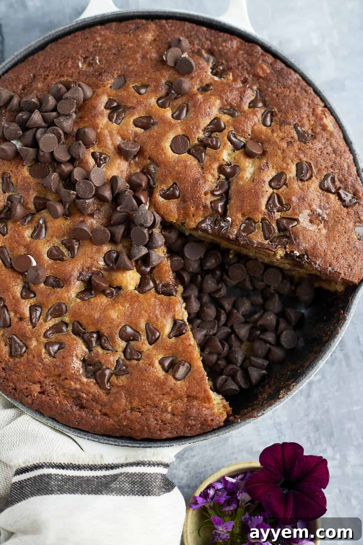Overhead shot of a chocolate chip banana bread skillet with one slice removed, revealing the gooey chocolate interior. The missing slice's spot is filled with extra chocolate chips.