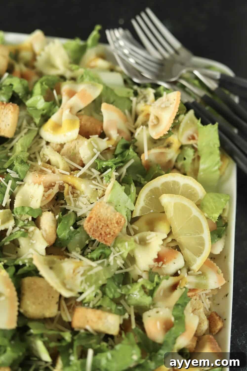 a white serving platter full of pesto pasta salad recipe with forks in the corner and lemon wedges on the side