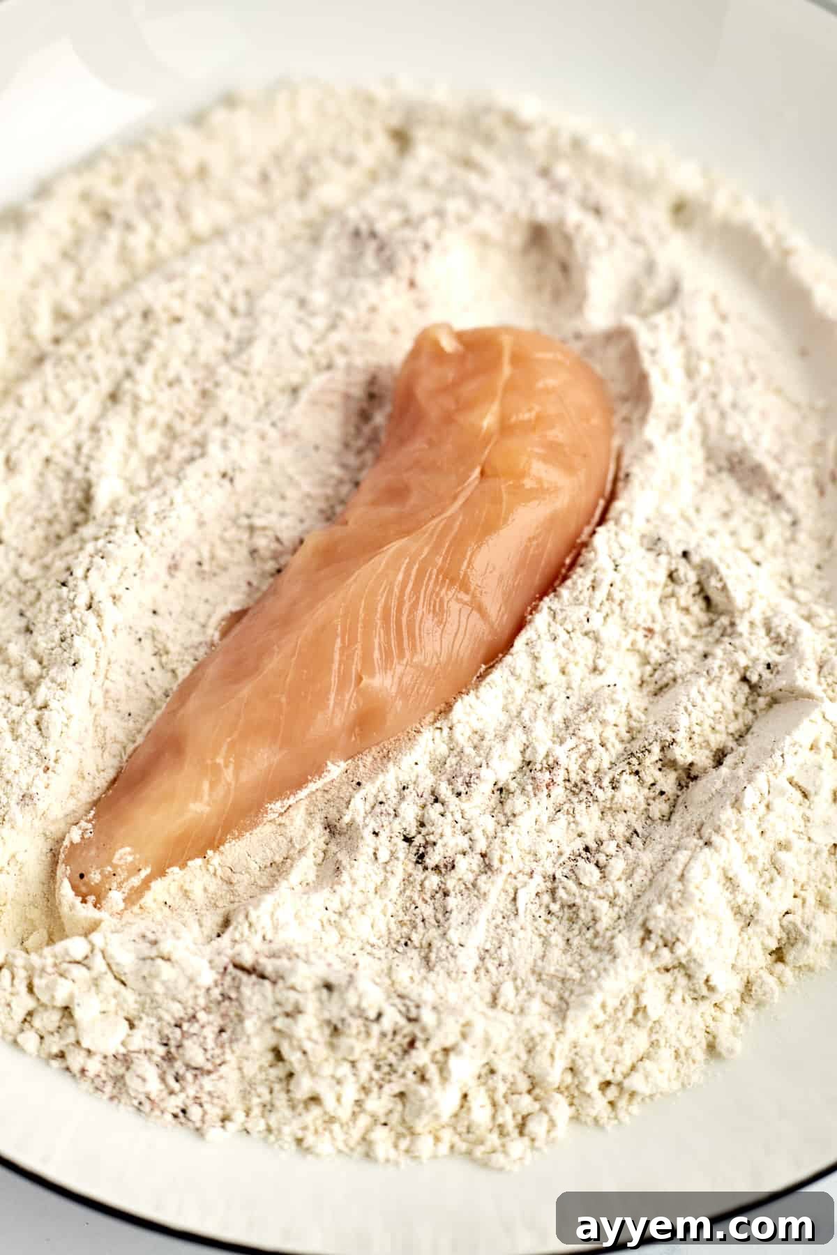 Island-Style Coconut Chicken Tenders 3 a raw chicken tender in a coconut breadcrumb mixture