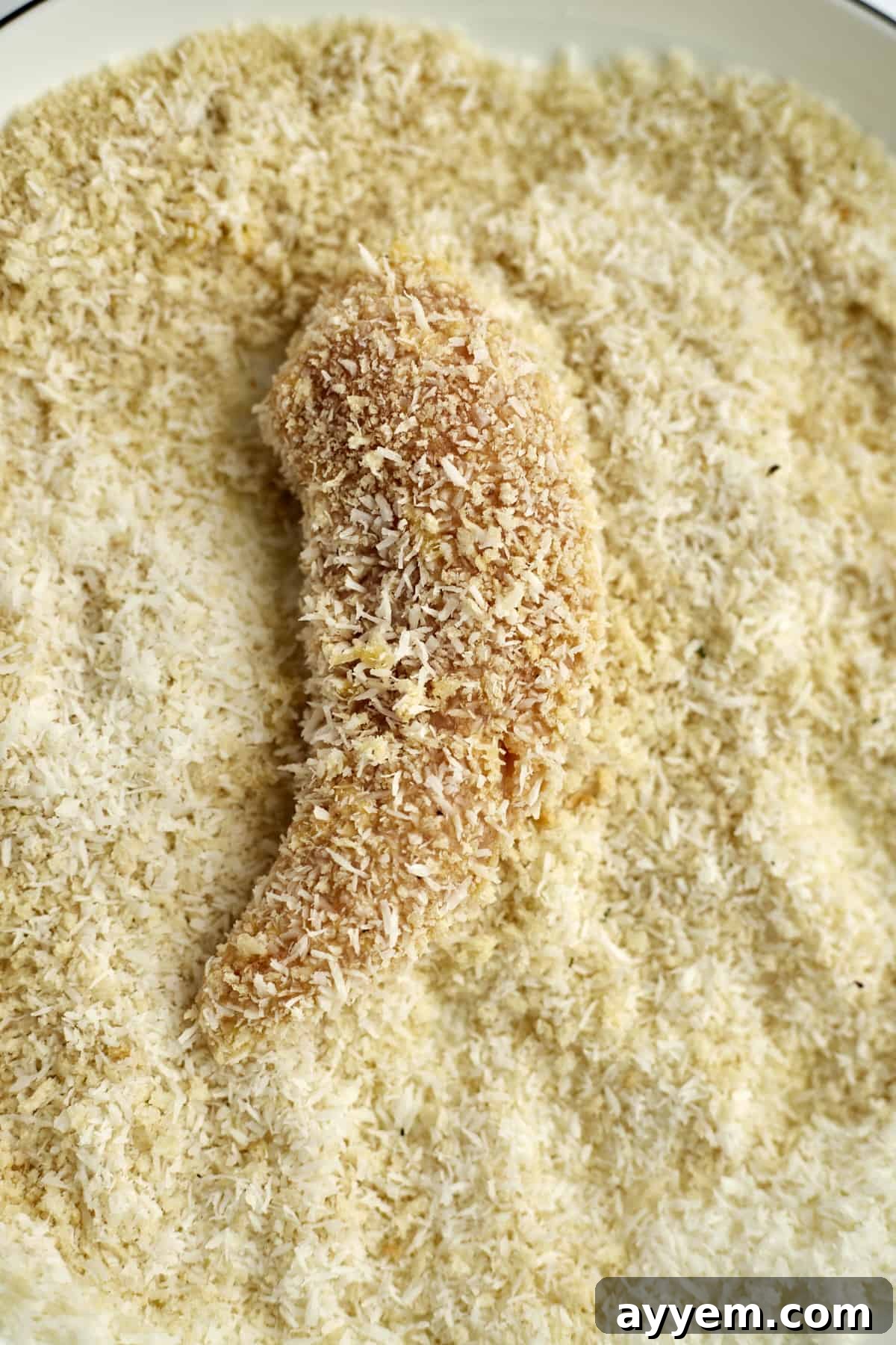 Island-Style Coconut Chicken Tenders 5 a raw chicken tender in a breadcrumb mixture