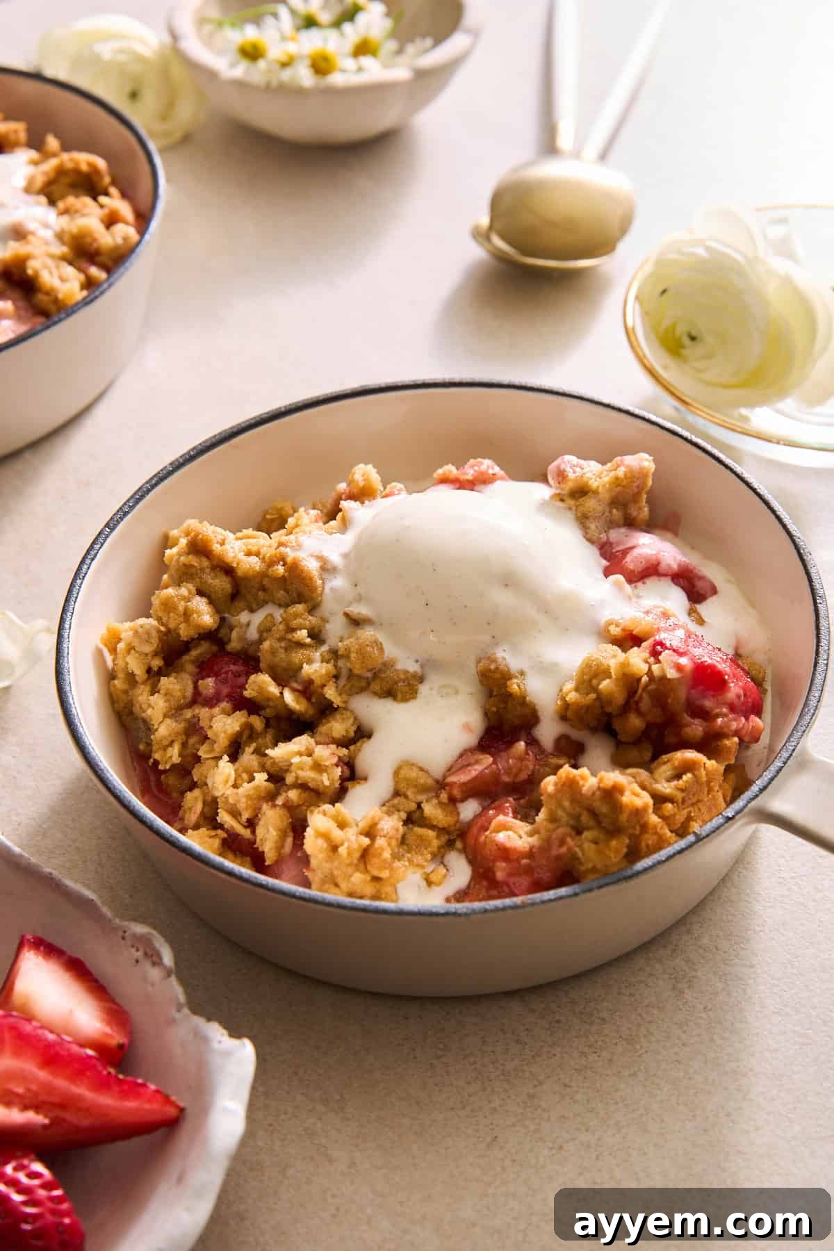 A bowl of strawberry crisp with oat topping topped with a scoop of vanilla ice cream.