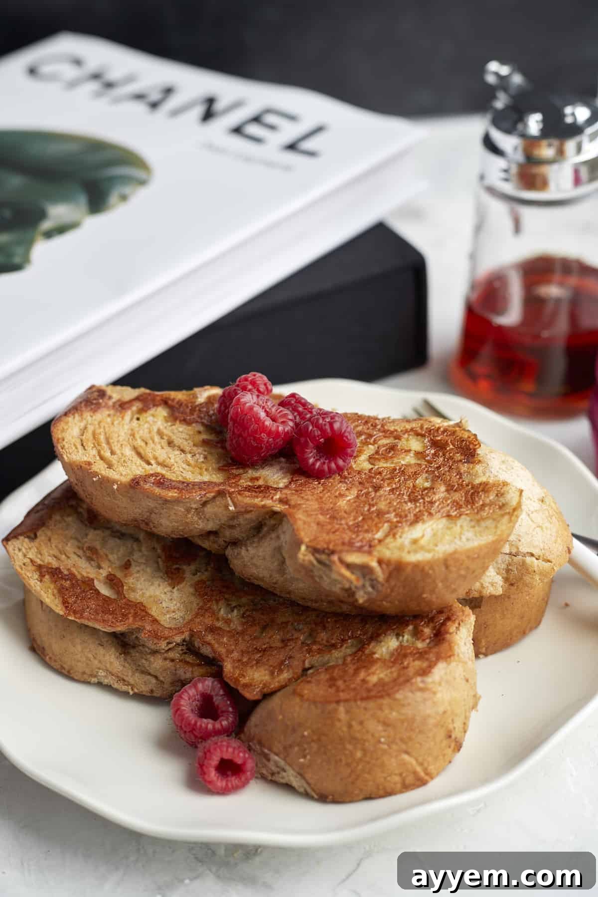 A serving of Sheet Pan French Toast adorned with fresh raspberries and a generous pour of maple syrup, on a white plate.
