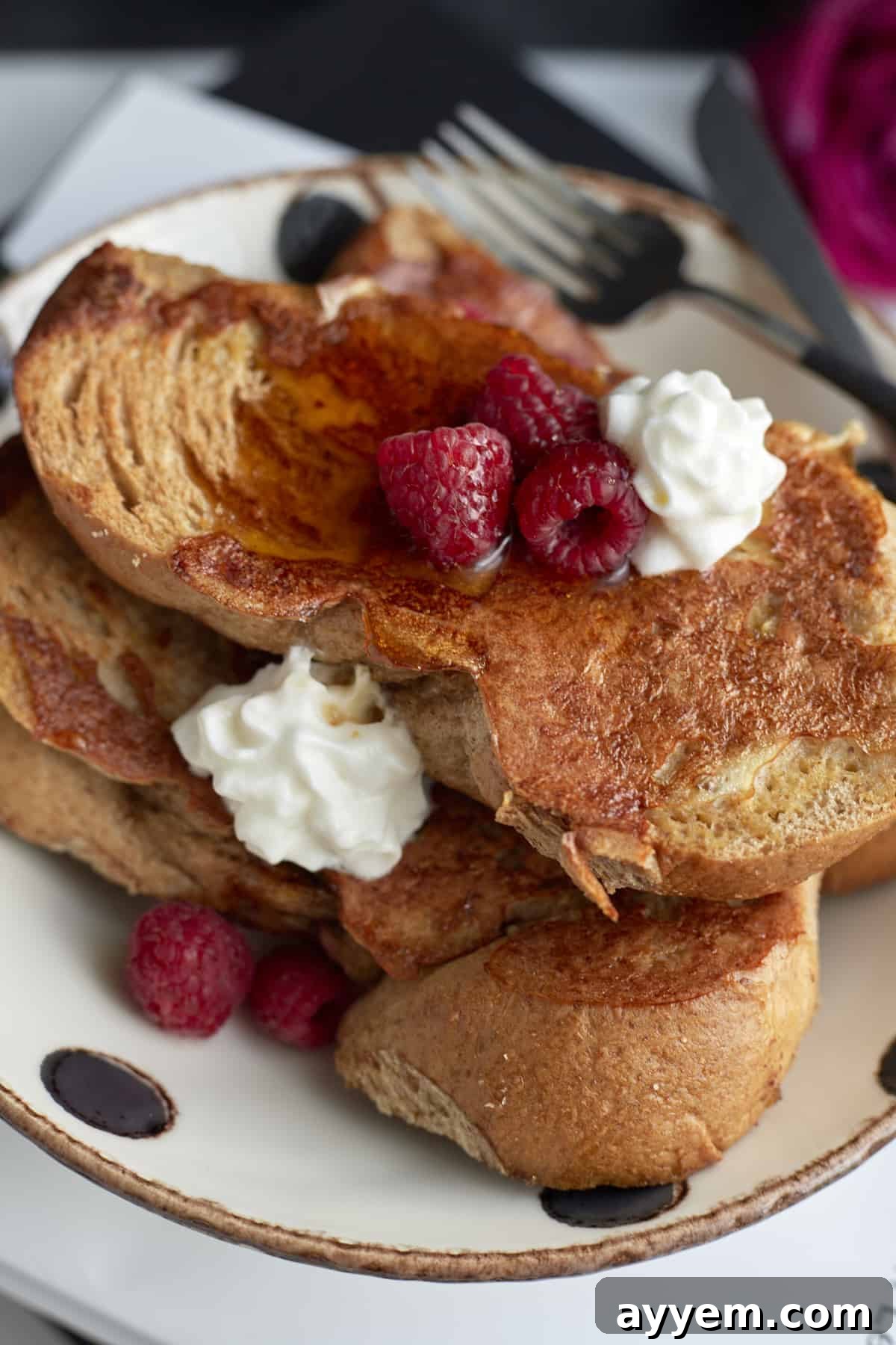 A stunning plate of Sheet Pan French Toast generously topped with fresh raspberries and a swirl of whipped cream.