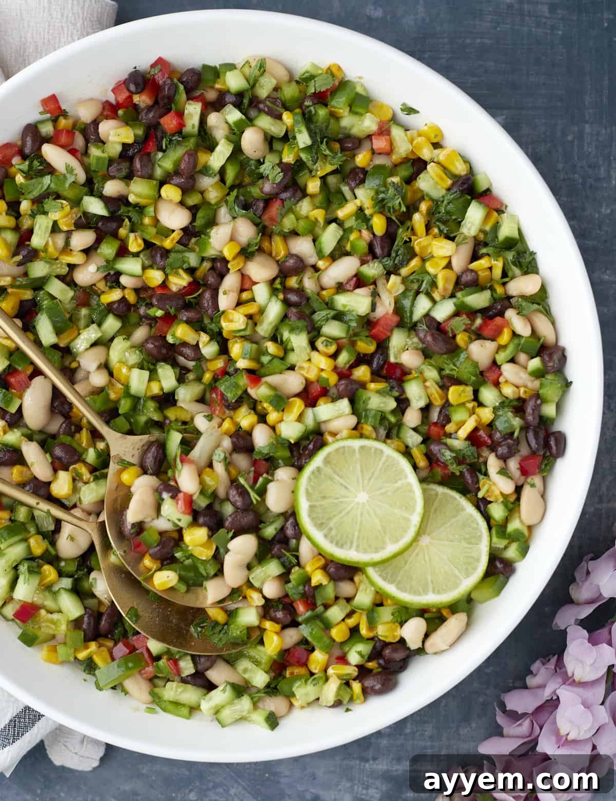 Large white bowl filled with freshly mixed cowboy caviar, garnished with lime wedges and golden serving spoons, ready to be enjoyed.