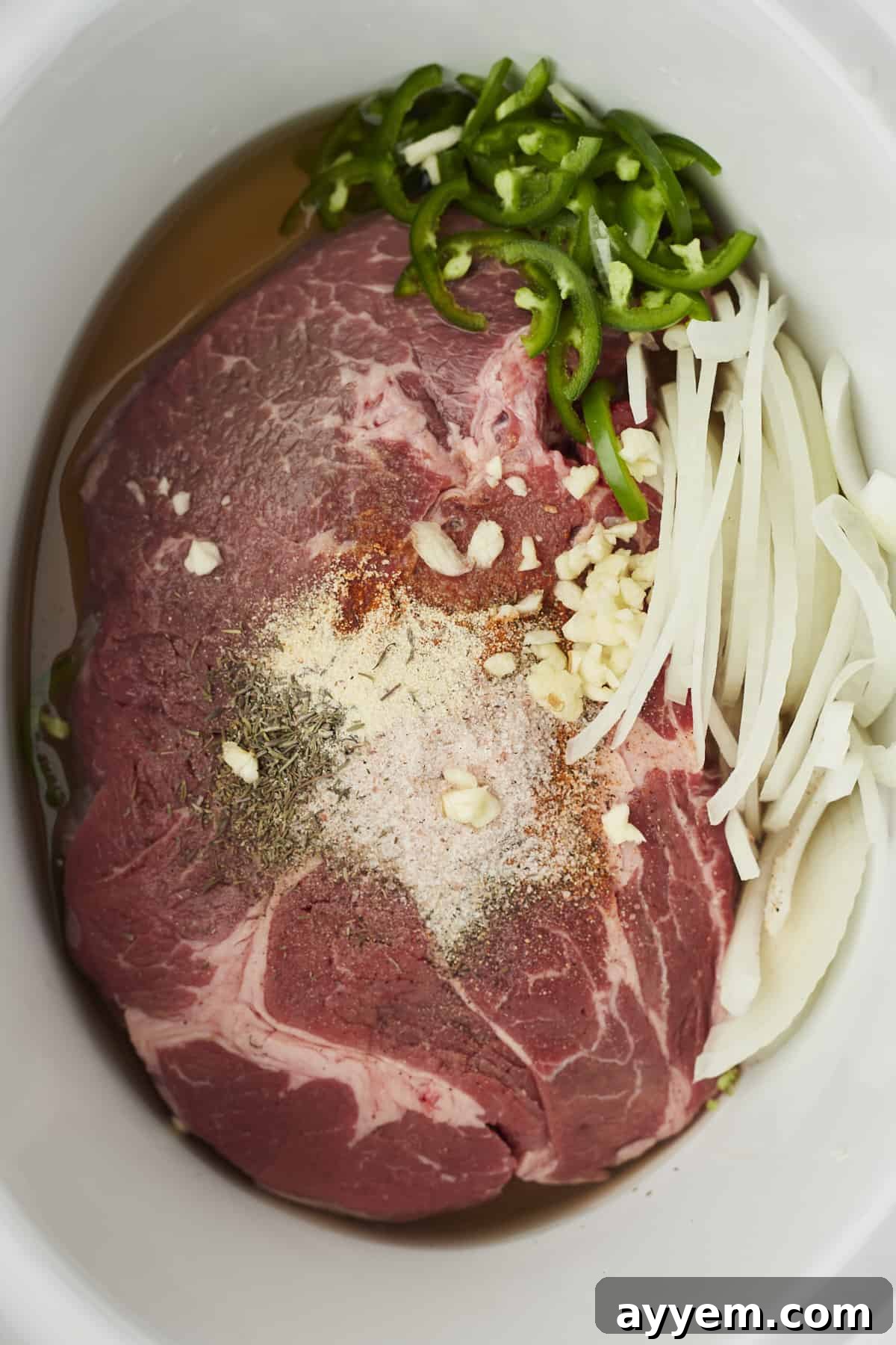Overhead shot of chuck roast, onions, garlic, jalapeños, and spices perfectly arranged in a slow cooker, ready to cook.