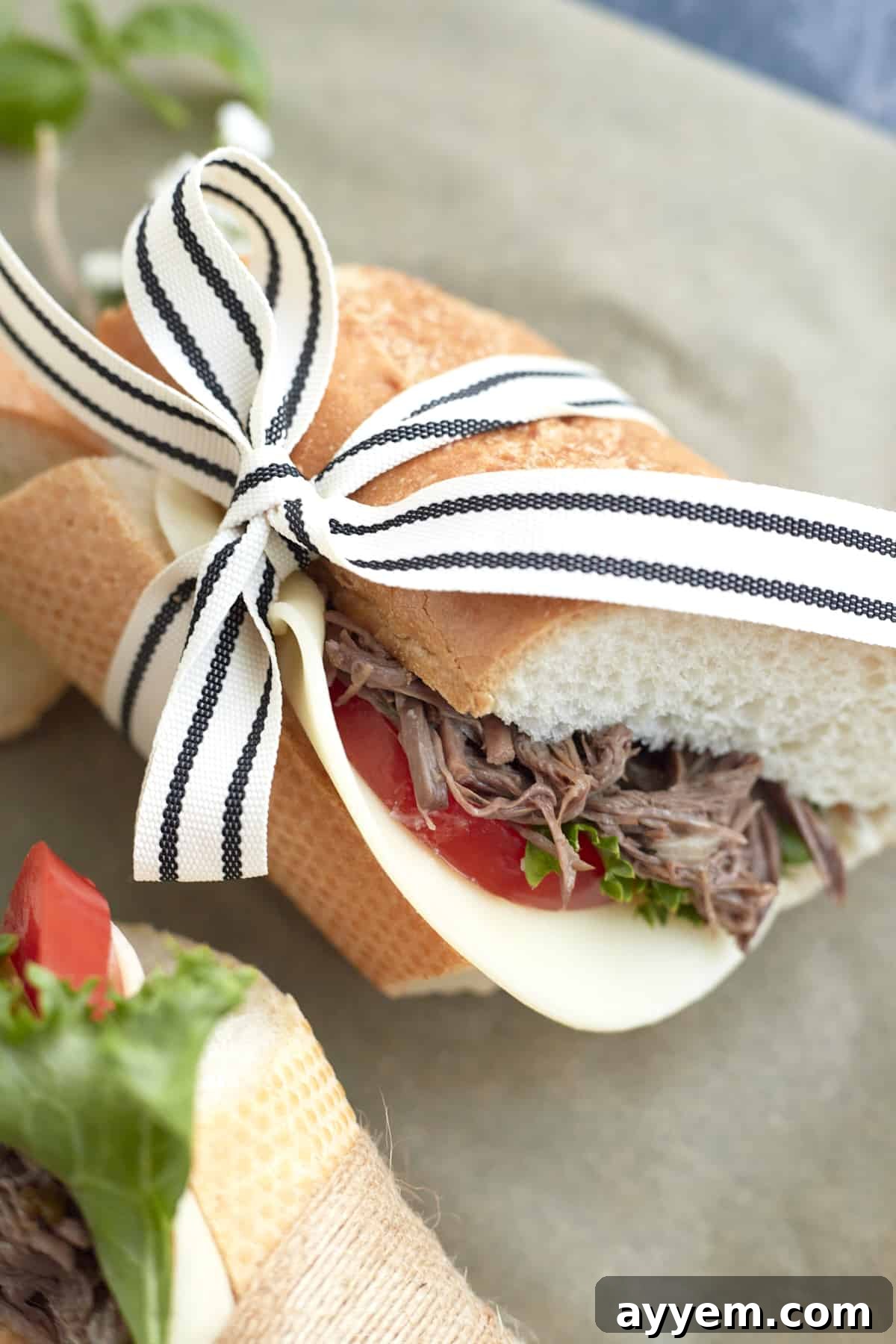 A single, perfectly crafted Po'Boy sandwich, tied with a ribbon, featuring tender beef, crisp lettuce, juicy tomatoes, and a slice of cheese.